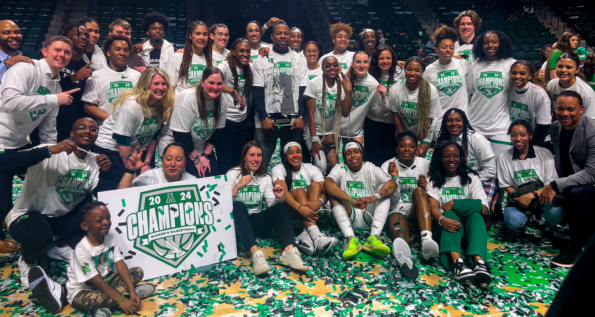 UNT Mean Green Women's Basketball team posing together on the court