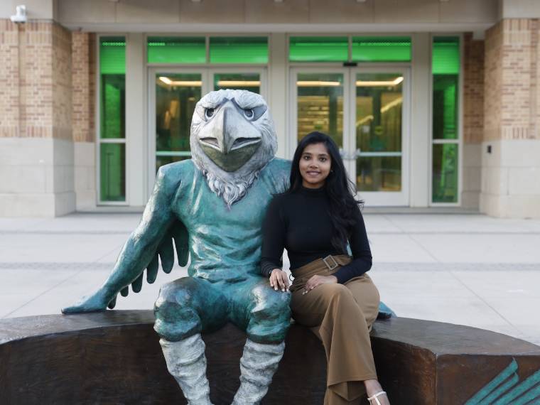 Kouschica Bosadi Ulaganathan sits next to the Scrappy statue in front of the UNT Union.
