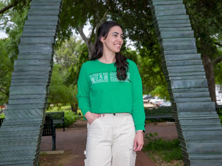 Rachel Trammel poses under the UNT library mall book arch sculpture.