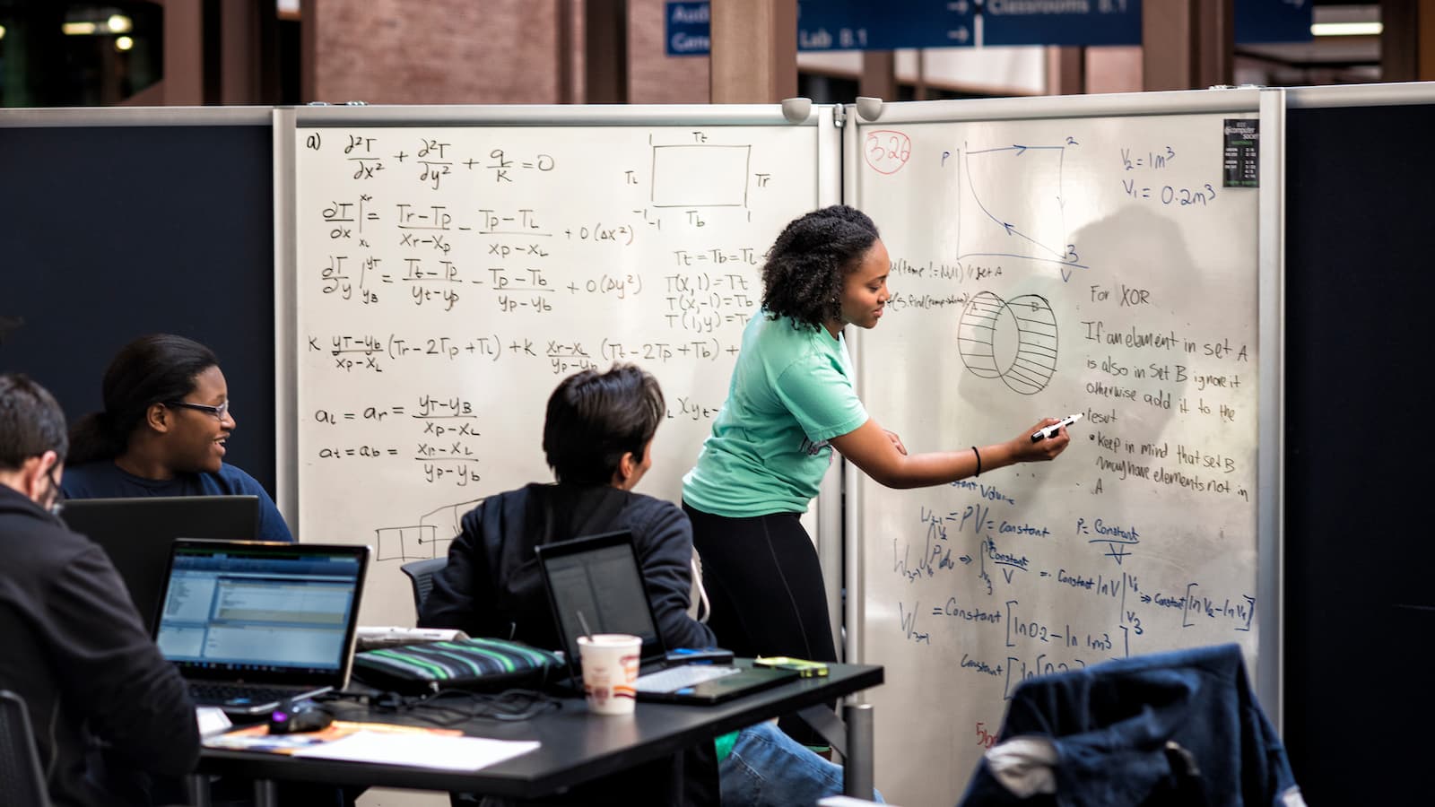 Students gathered around a whiteboard as an instructor demonstrates an equation