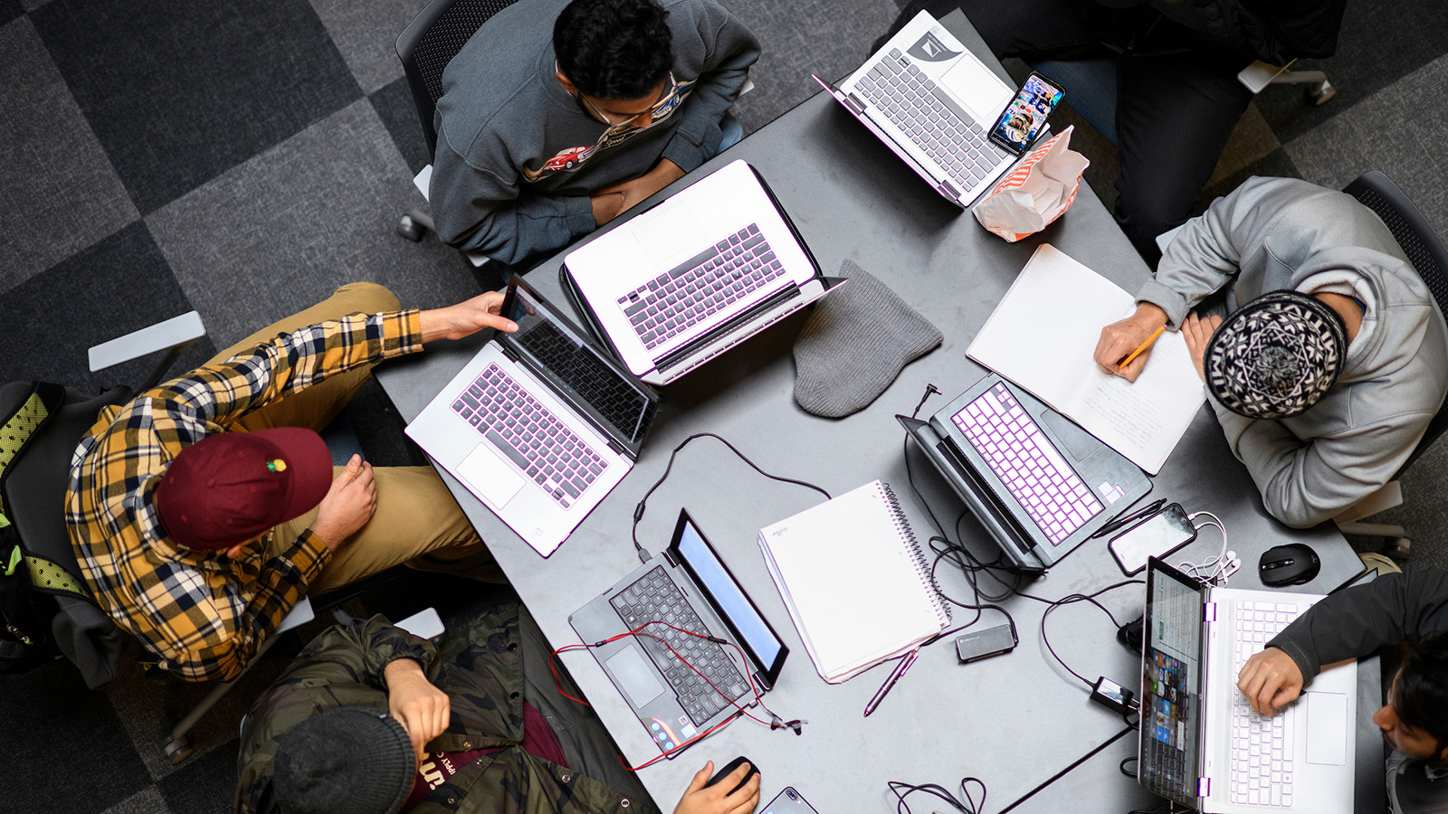 Overhead view of students working with laptops at a table. 