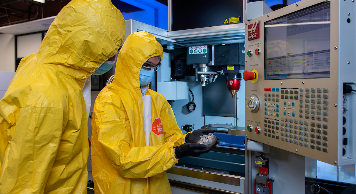 Two people in yellow protective gear work at the UNT Center for Agile and Adaptive Manufacturing