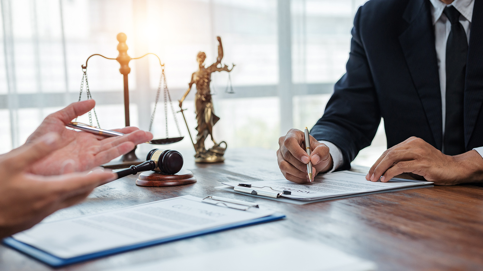 Photo of two people in suits with legal documents and a Lady Justice statuette in the forground