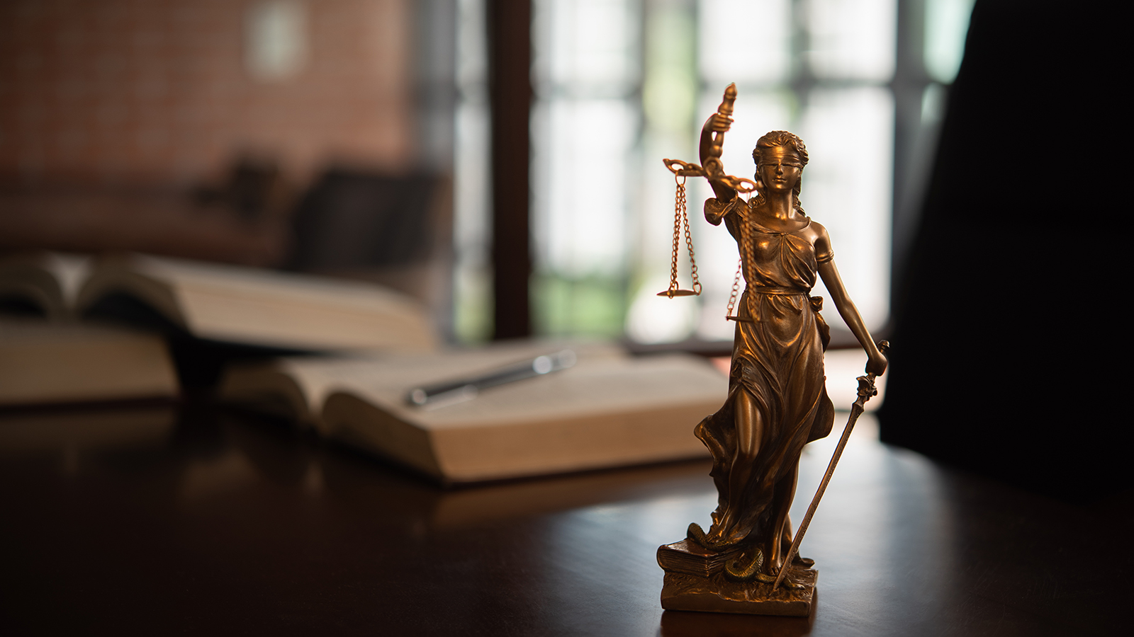 Legal texts on a desk with a Lady Justice statuette in the forground