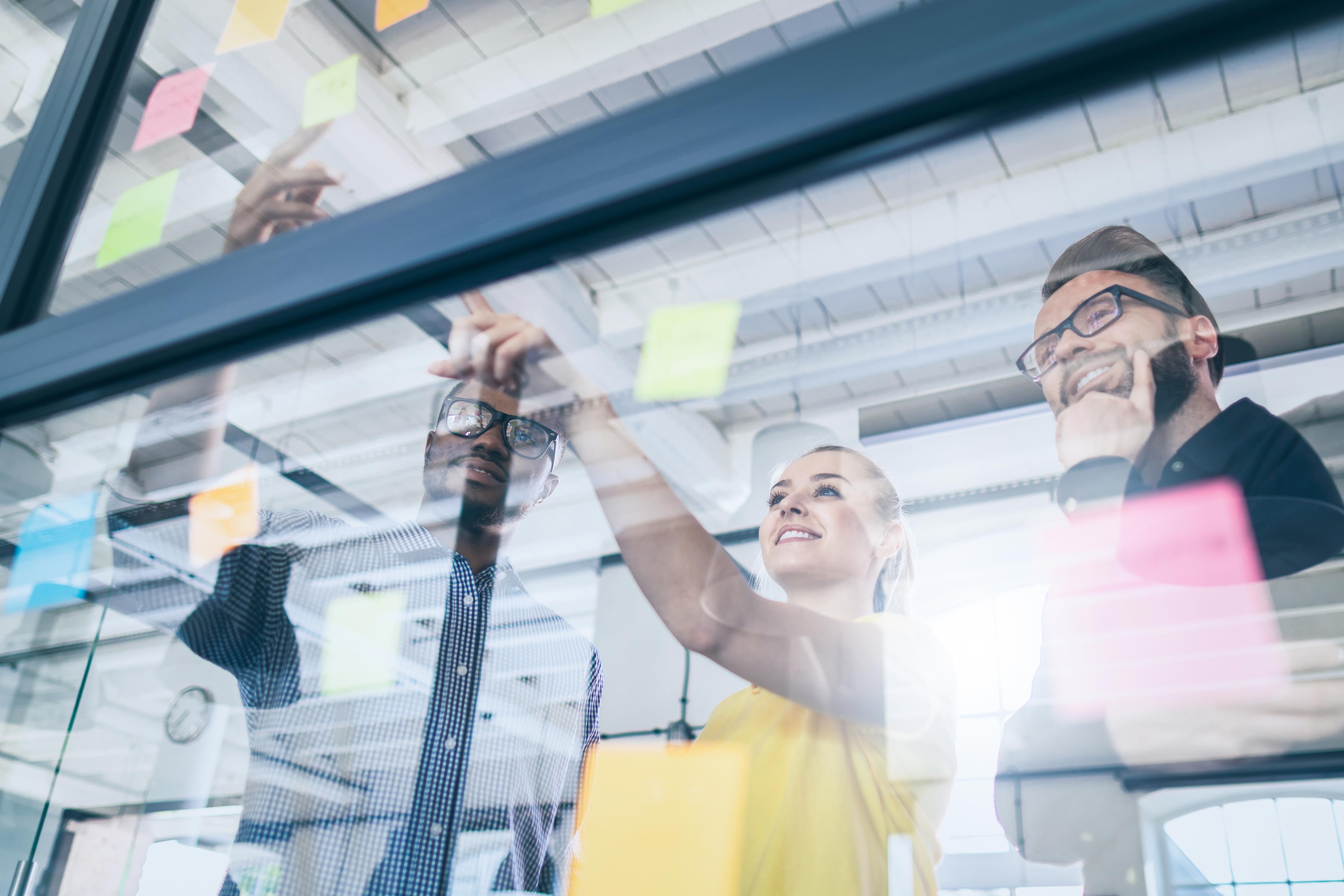 Three business people pointing at a a whiteboard with post-its
