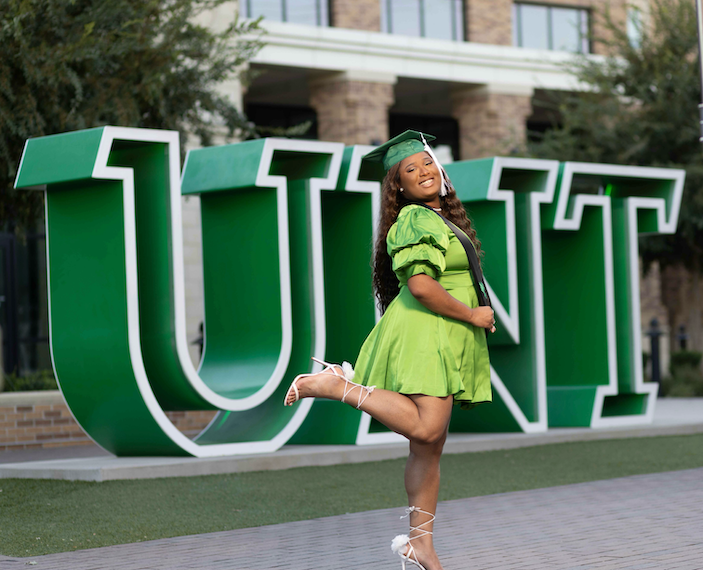 Fall 2024 grad Shanice Parker poses in front of the UNT Welcome Center sign
