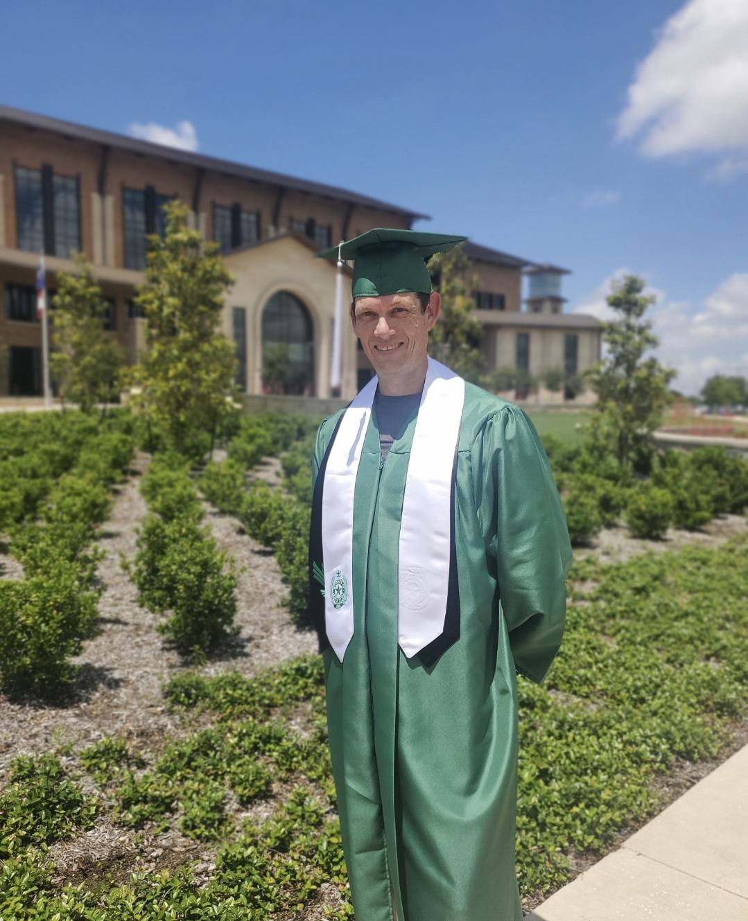 Flip Flippin wears commencement regalia and poses in front of UNT at Frisco