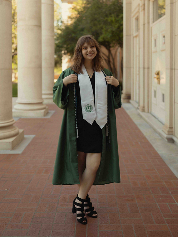 Paige Sanders poses on campus in green commencement regalia