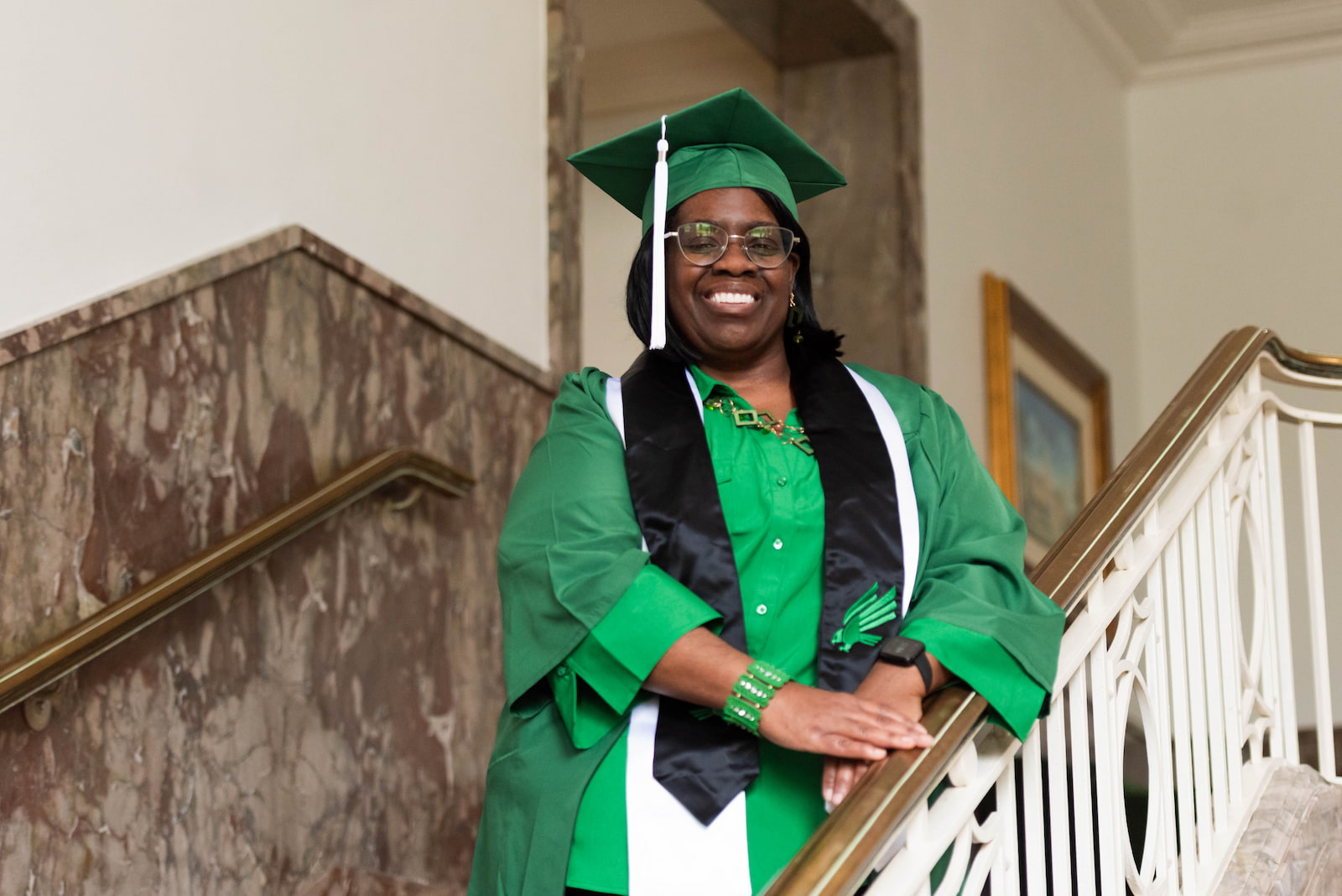 Photo of Brenda Hill posing on a staircase wearing Commencement re