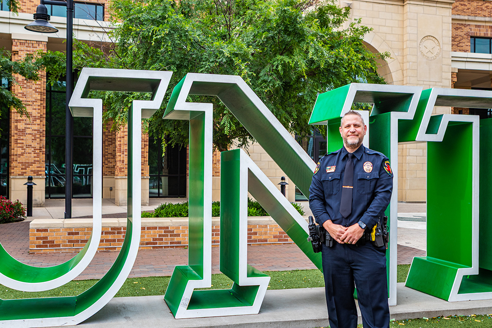 Kevin Crawford poses in police uniform next to the UNT Welcome Center sign