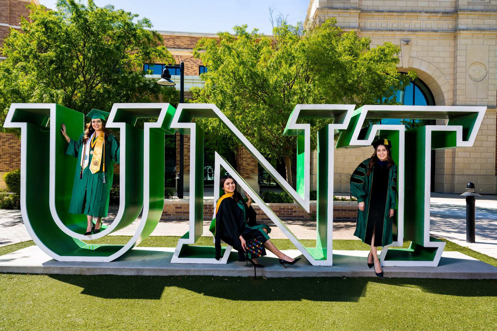 UNT Graduate Lina Rodriguez smiling and posing in regalia inside the campus UNT letters
