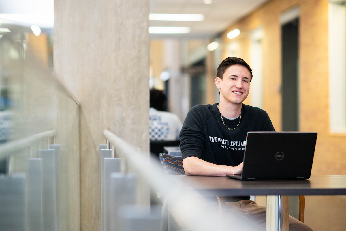 Person smiling at camera sitting at a table with laptop open