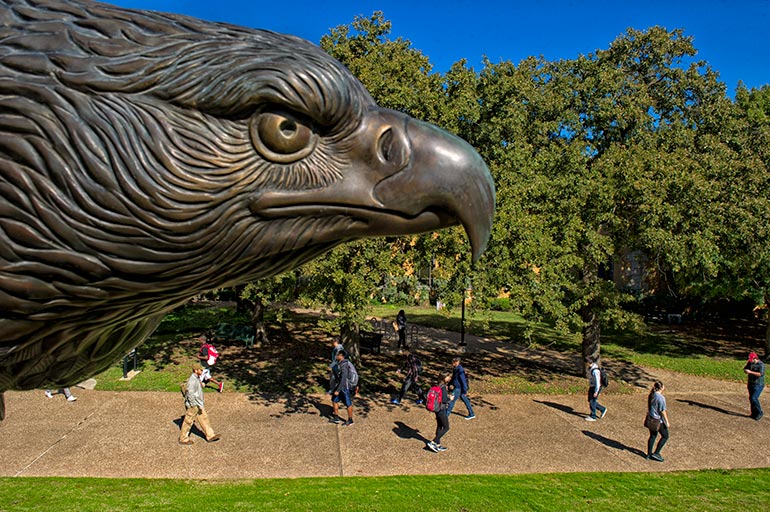 Students walking on campus with bronze flying eagle statue in the foreground