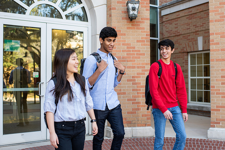 Three UNT students leaving a campus building with smiles on their faces.