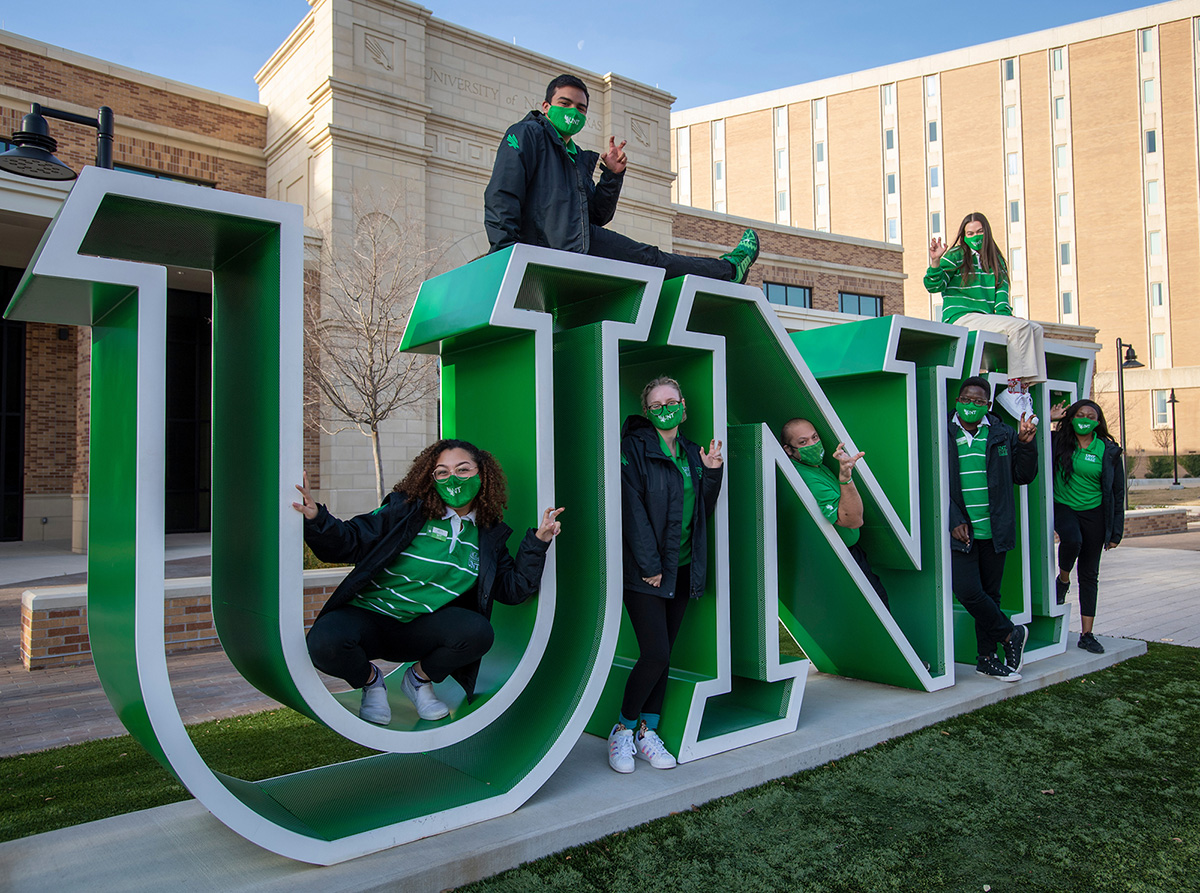 Several students posing with the life size UNT sign outside the welcome center.