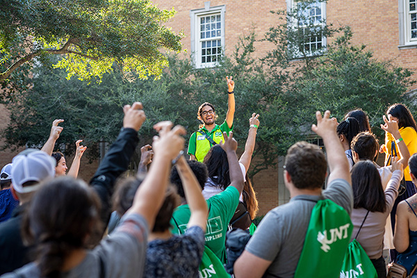 Orientation leader holding up the UNT hand sign with a group of students. 