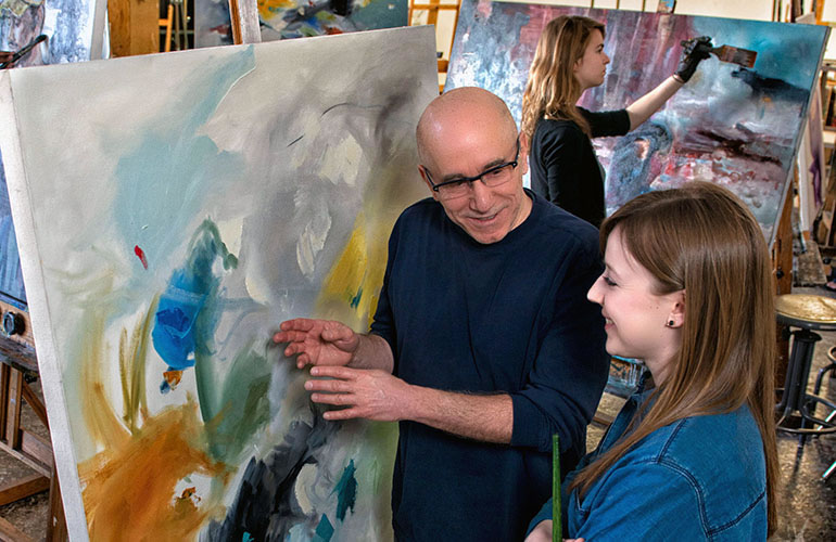 Professor and student in a painting studio looking at a canvas.