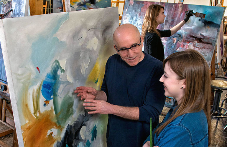 Professor and student in a painting studio looking a a canvas.