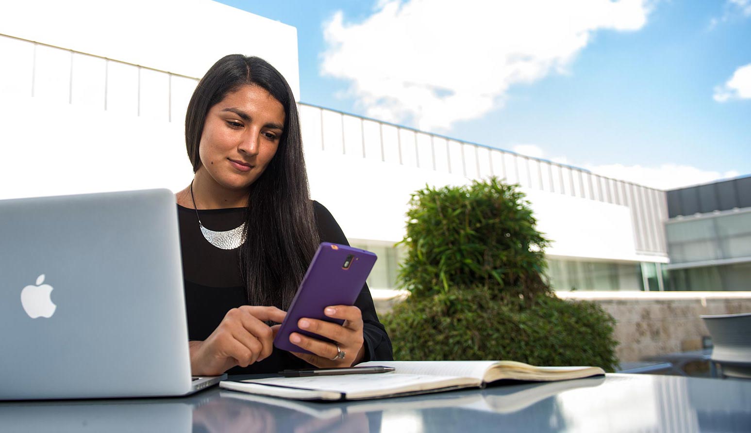 Student studying outside with laptop and cell phone.