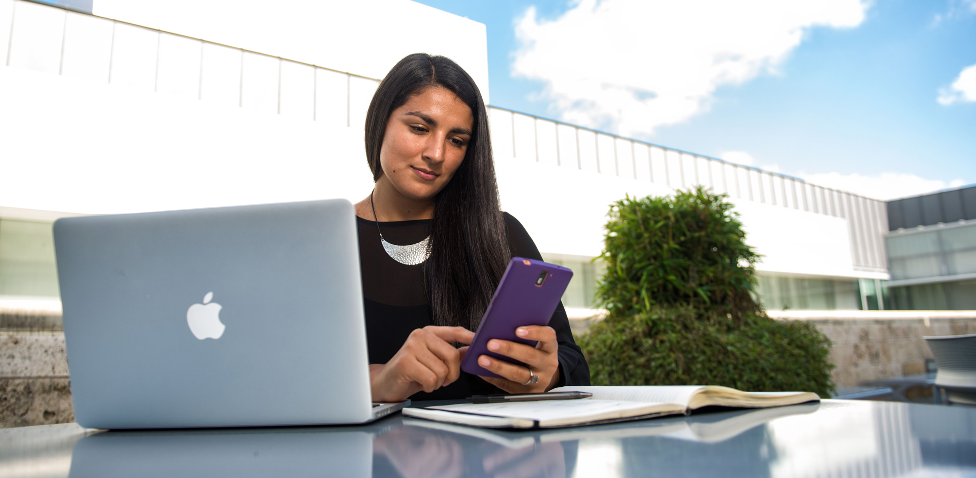 Student looking at their cell phone, with laptop open on a table.