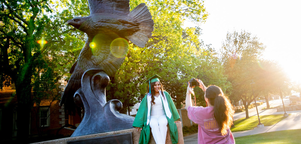 Student in regalia posing with eagle statue