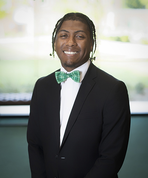 Man wearing a blazer and green bowtie smiling. 