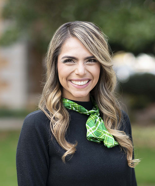 Woman wearing a black blouse with a green tie smiling. 