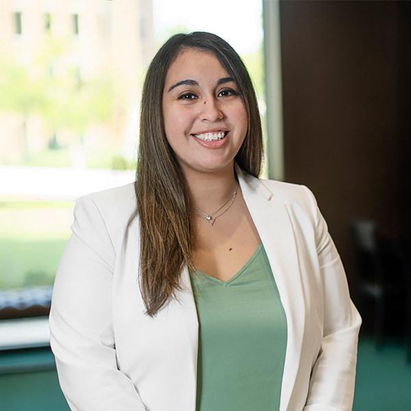 Woman wearing a green shirt and white blazer and smiling. 