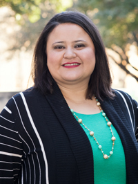 Woman wearing a green blouse and blazer smiling. 