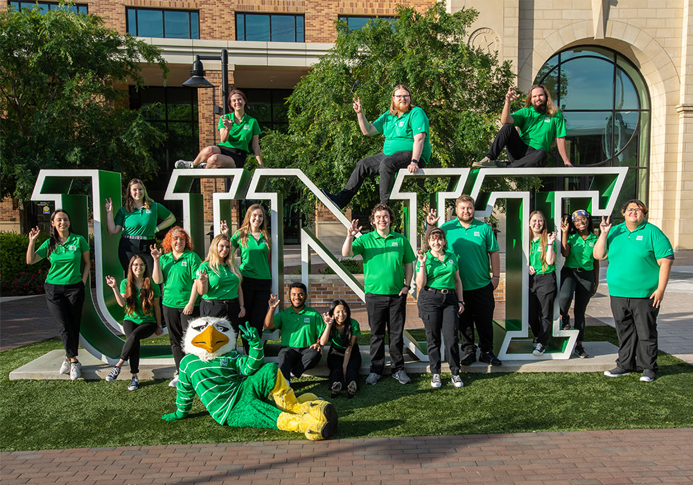 UNT Admission Recruiters posing in front of a UNT sign with Scrappy mascot.