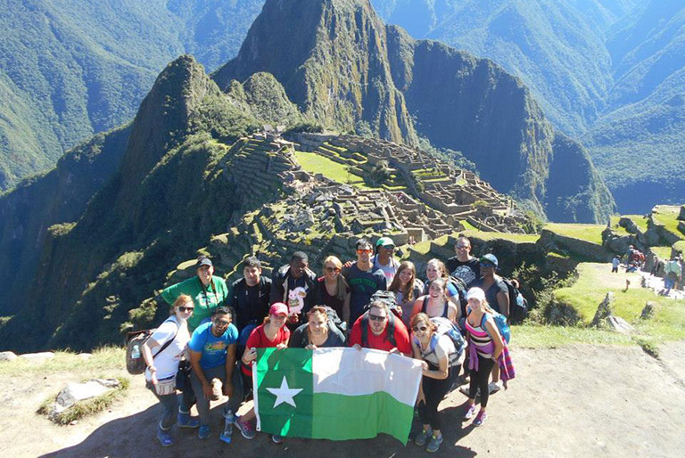 A group of students holding a UNT flag on a mountain top.